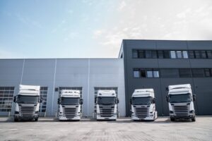 Line of new modern white trucks parked outside a sleek, industrial warehouse, ready for logistics or transportation services