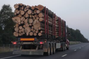Wood truck with three-axle semi trailer drive on asphalted suburban one way road
