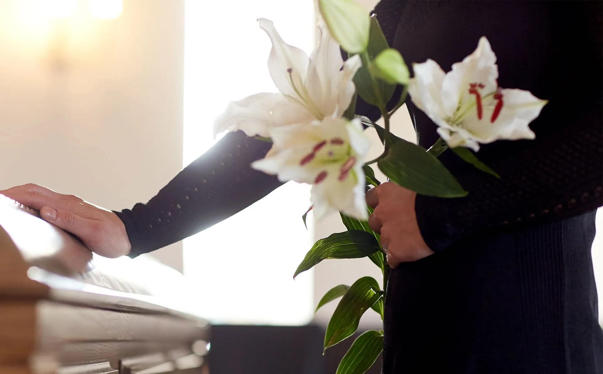 person holding flowers with hand on coffin