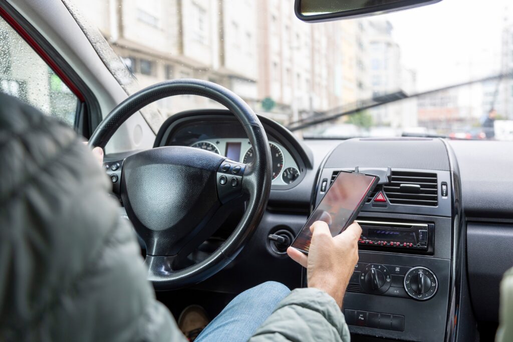 Driver using smartphone while behind the wheel of a car, representing distracted driving and road safety risk.