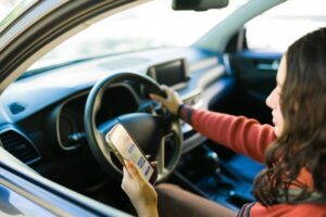 Female teenage driver using a smartphone while behind the wheel, highlighting the dangers of distracted driving.