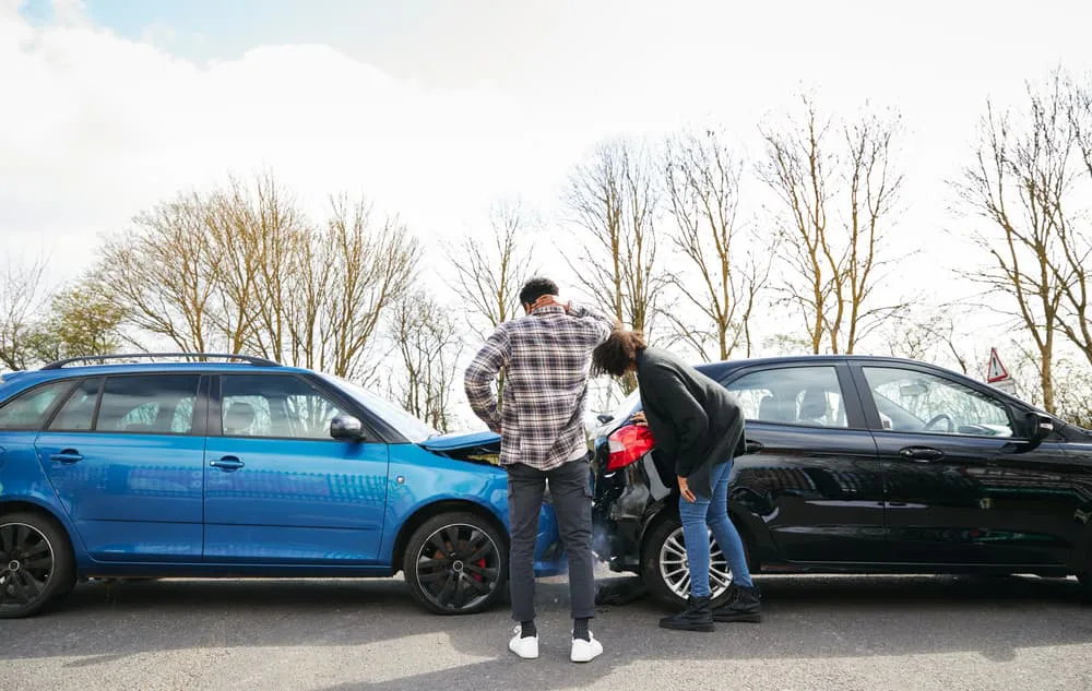Young male and female drivers looking at damaged car hit from behind after traffic accident.
