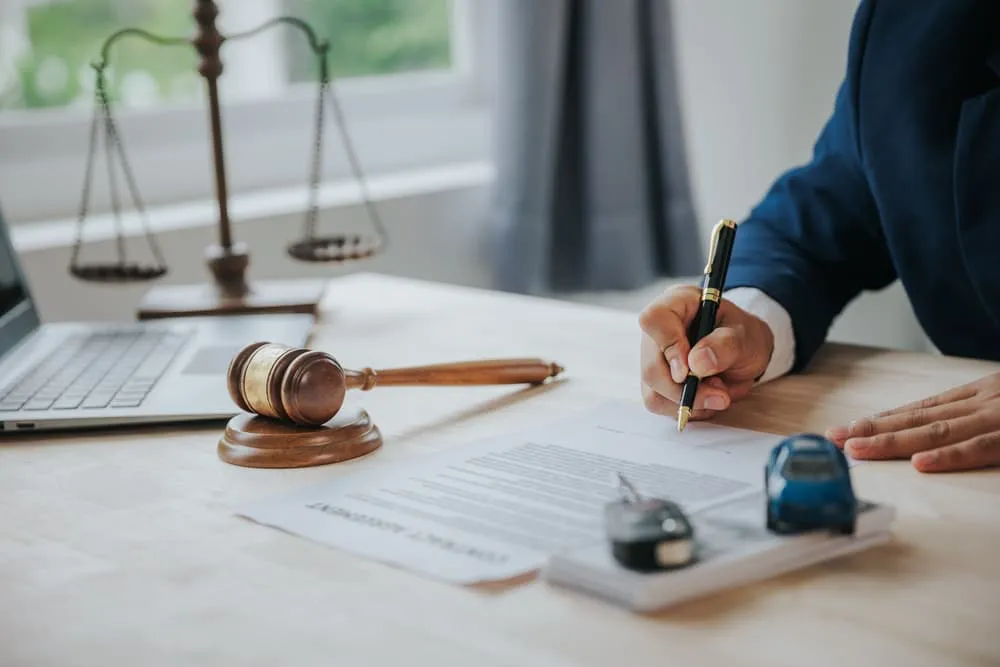 Lawyer reviews car accident liability documents with gavel, scales, car keys, and toy car present.