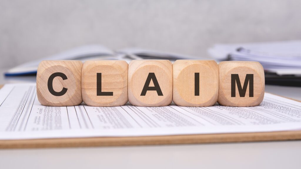 Wooden blocks spelling the word claim on a desk with documents and papers. Wooden blocks spelling the word claim on a desk with documents and papers.