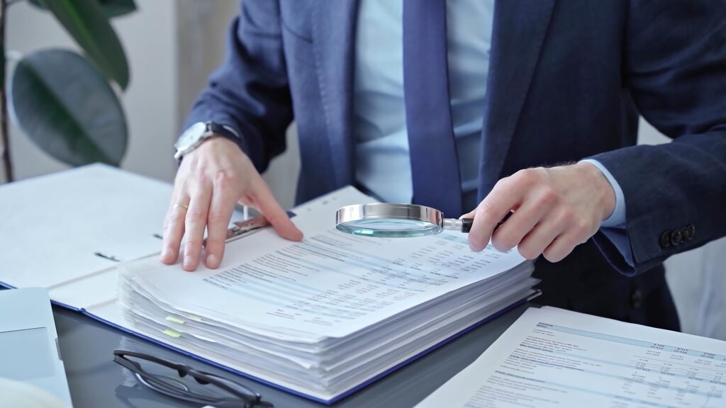 Business professional reviewing financial documents with magnifying glass, representing audit, investigation, or legal analysis.