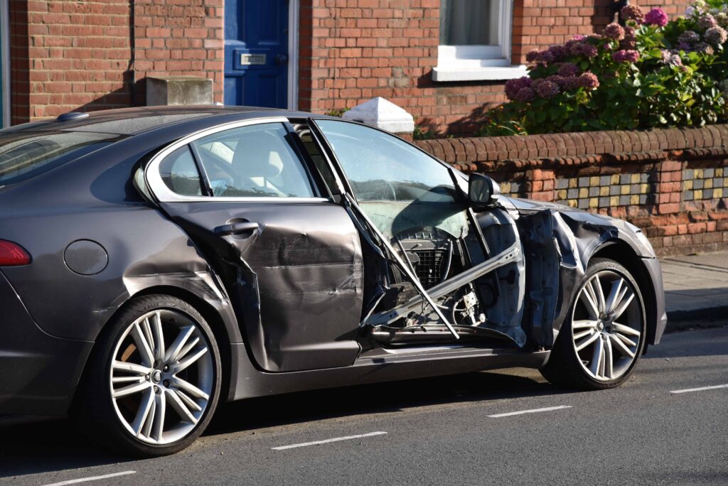 Car with severe side damage after collision parked on residential street, representing auto accident and vehicle repair claim.