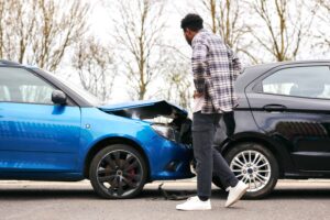 Man inspecting car damage after rear-end collision between blue and black vehicles, representing car accident and injury claim.
