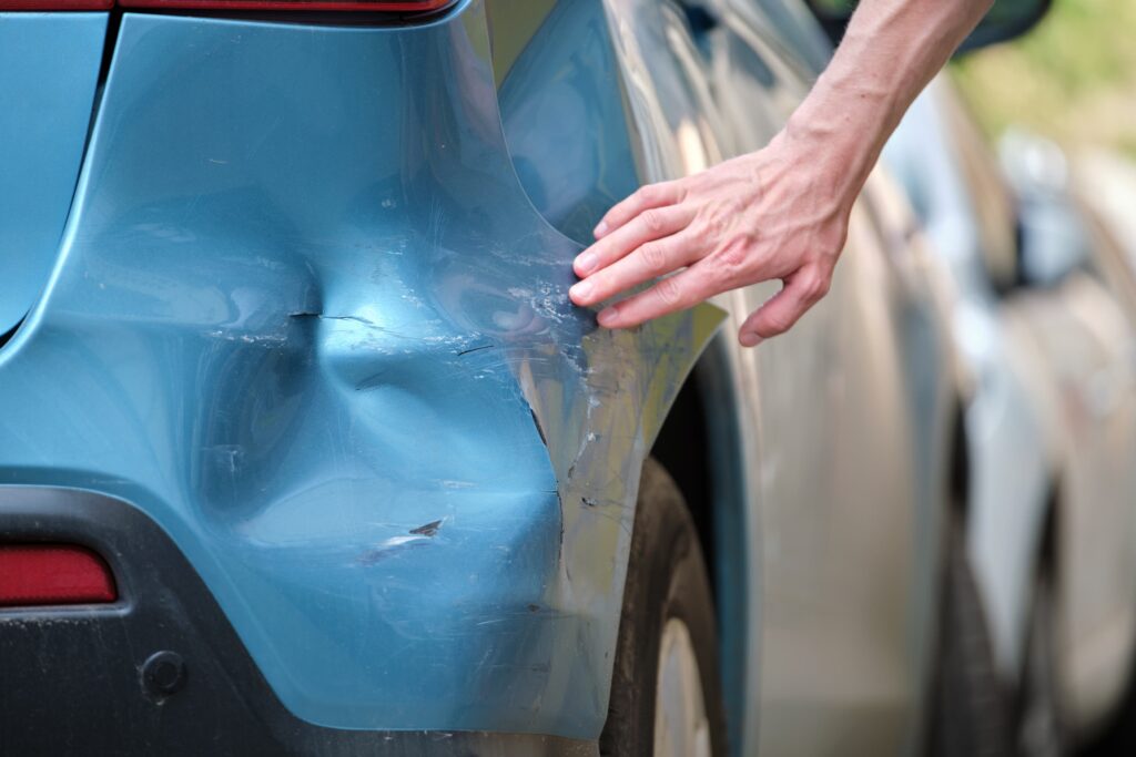 Close-up of person inspecting dent and scratches on blue car bumper after minor accident, representing vehicle damage and repair claim.