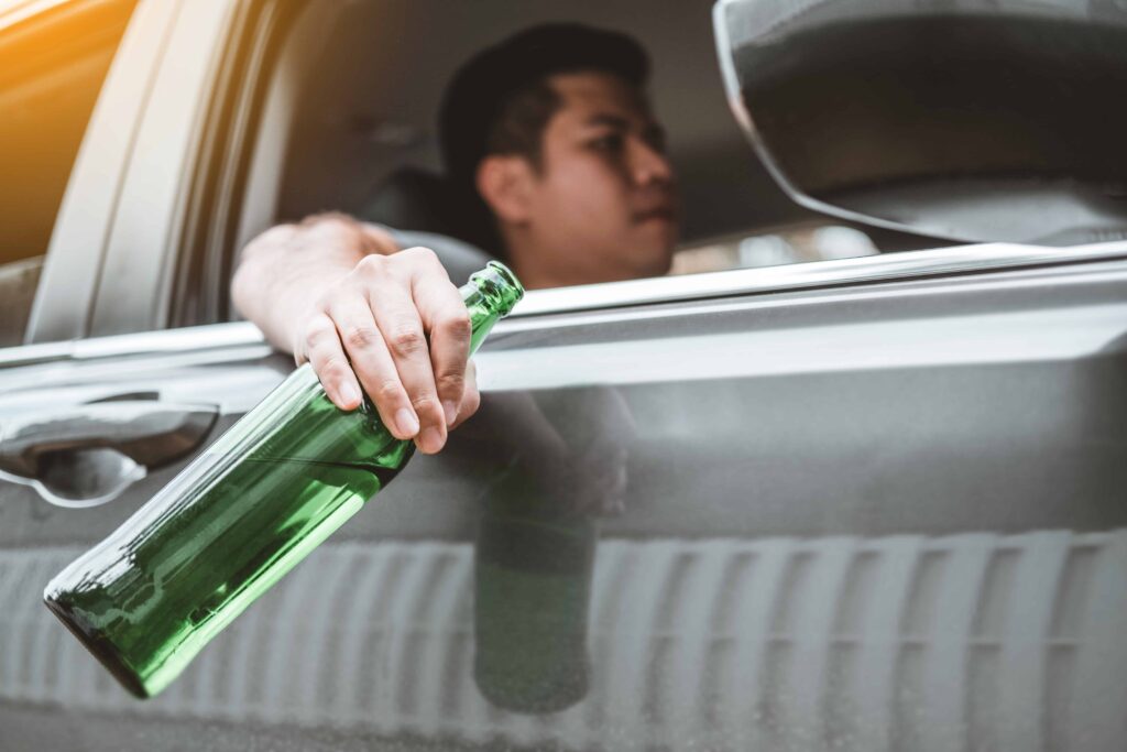 Driver holding beer bottle out of car window, representing drunk driving and DUI law enforcement risk.