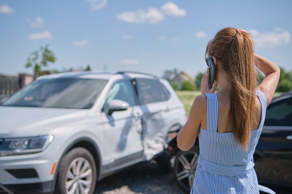 Woman Calling for Assistance After Side-Impact Car Accident Woman calling for help after a car accident while inspecting side-impact damage on her SUV.