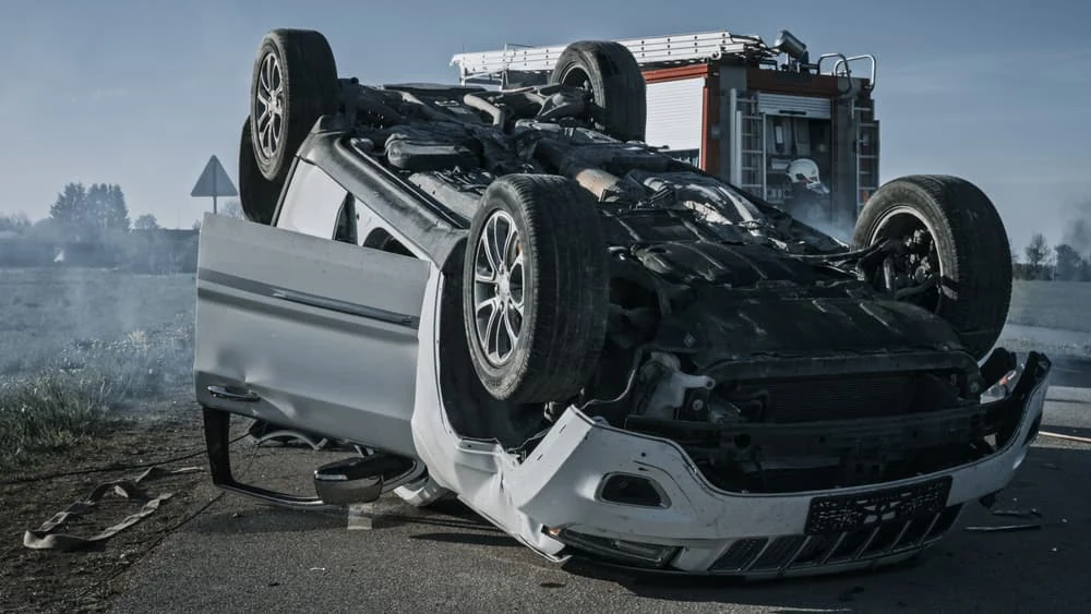 Silver car overturned on its roof at the side of a road after a crash